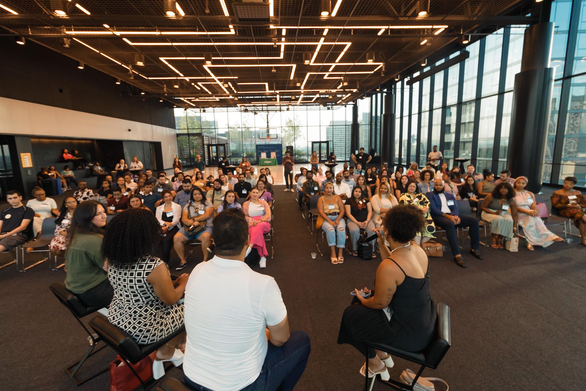 Group of people listening to a panel discussion with panelists seated on stage.